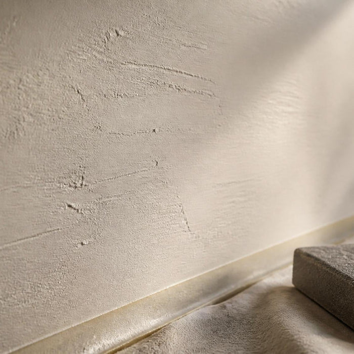 Close-up van gestucte muur met kleine oneffenheden die zichtbaar worden in strijklicht.