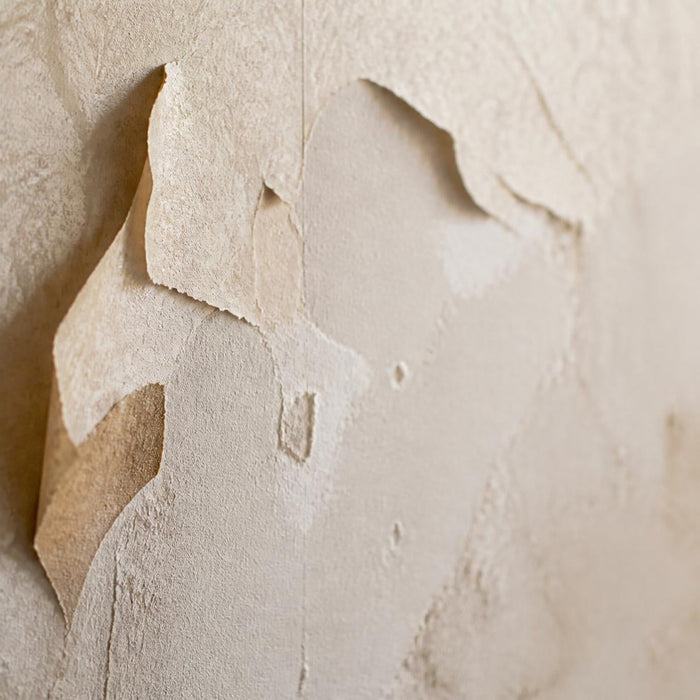 Close-up van loszittend behang met naden en blaasvorming op een muur.