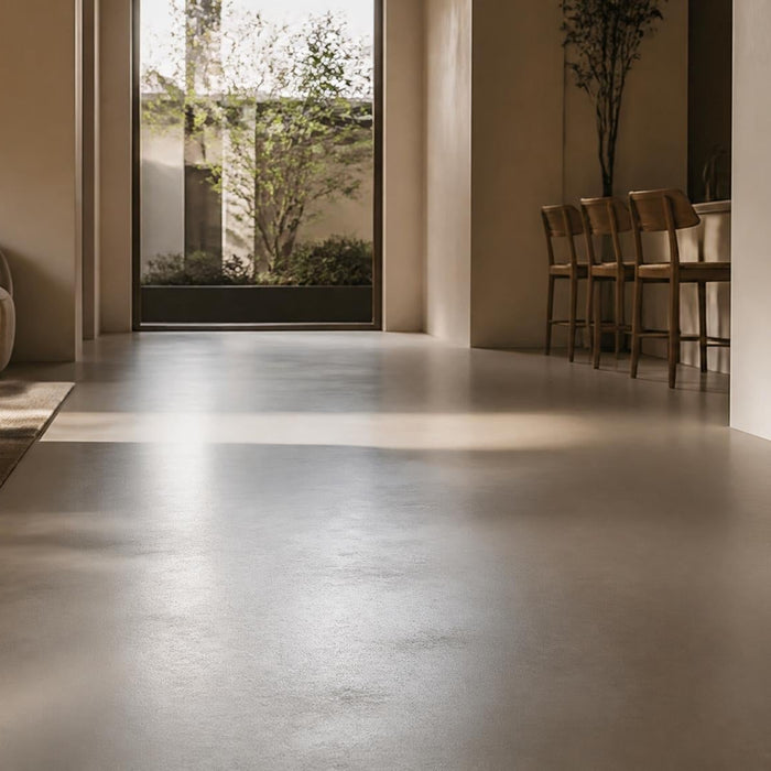 Moderne woonkamer met gietvloer in warm daglicht, waarbij subtiele gebruiksschade en herstel aan de vloer zichtbaar zijn.